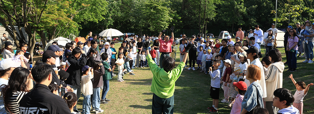 가면을 쓴 공연자가 풀이 우거진 길을 걸으면 퍼포먼스를 하고있다.